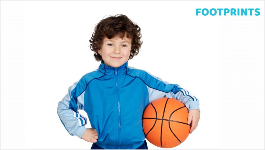 A young boy in a blue sports jacket holding a basketball, smiling confidently with his hand